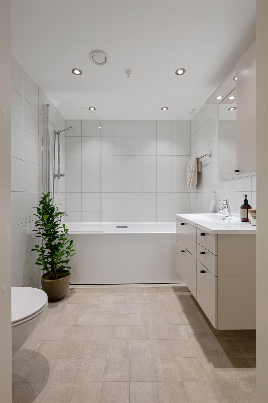 Badet består av badekar, dusjbatteri tilkoblet veggmontert hånddusjvegghengt servantskap med skuffer, ovenpåliggende servant, vegghengt toalett, speil, overlys og stikkontakt på vegg over servant. Nedsenket himling med malt flate og downlights Galleribilde