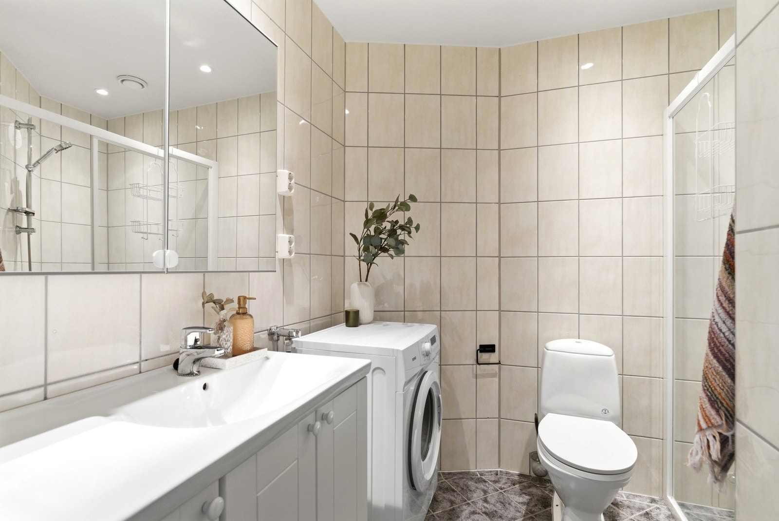 Flislagt bad innredet med opplegg for vaskemaskin helstøpt servantinnredning og speilskap montert på vegg- Downlights i himling Galleribilde