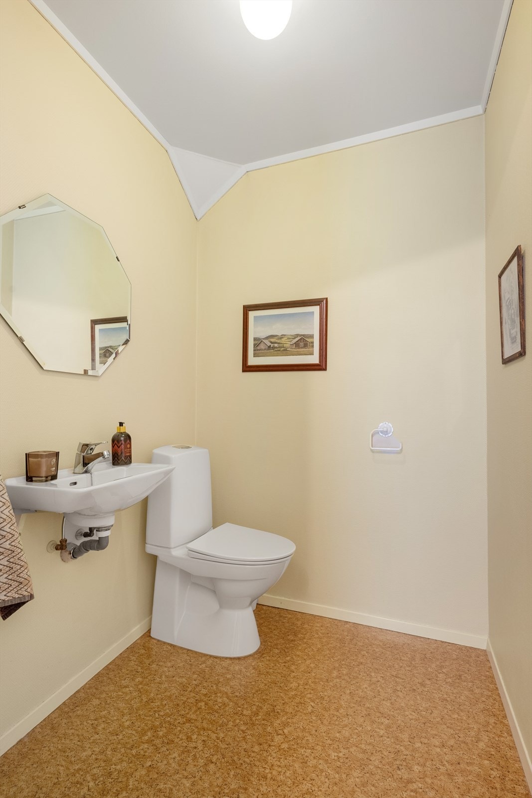 Praktisk toalettrom som innehar toalett og veggmontert håndvask med speil over. Galleribilde