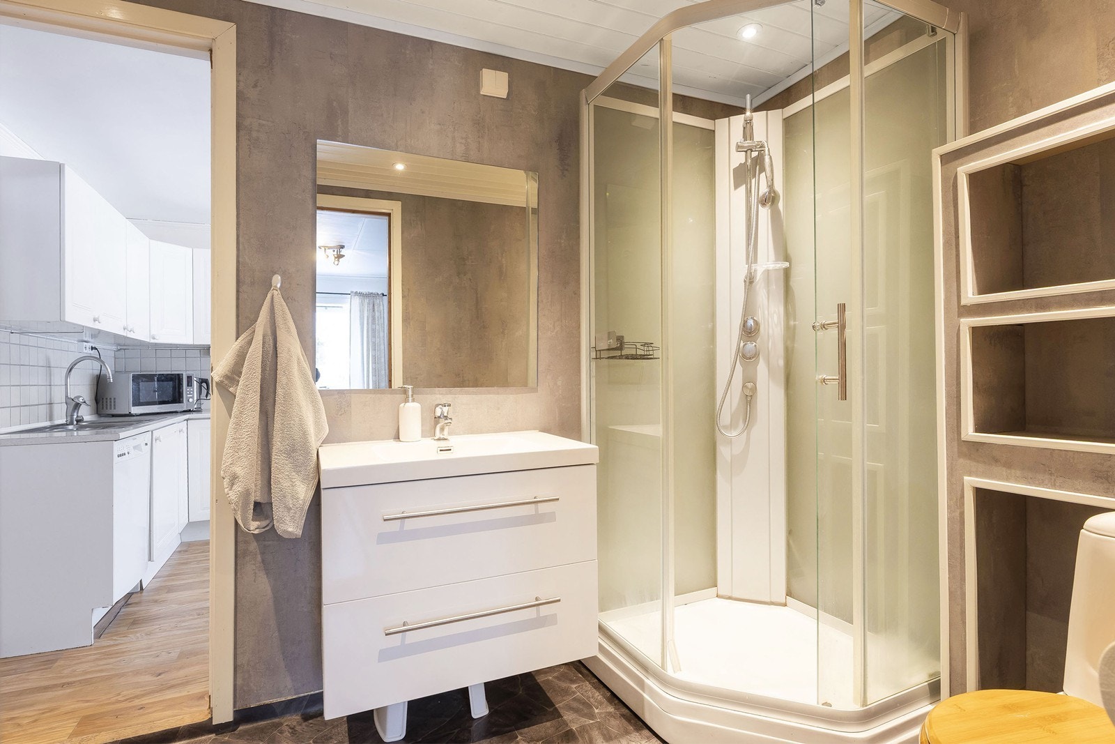 Badet har fine grå og hvite detaljer, pent innredet med servantseksjon med skuffer og romslig dusjkabinett Galleribilde