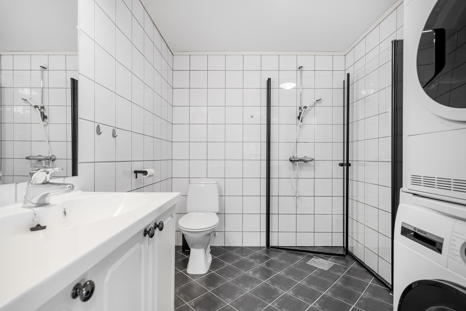 Flislagt bad med dusjhjørne, gode overflater med praktisk opplegg for vaskemaskin og tørketrommel. Galleribilde