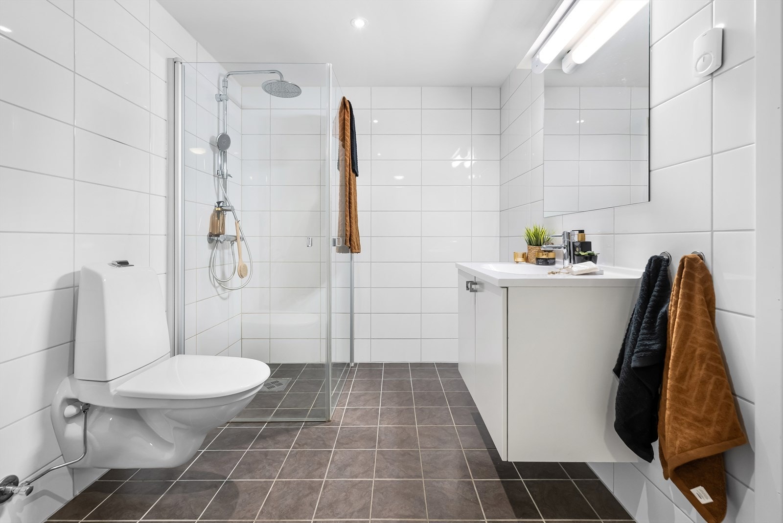 Det er innredet med servant, veggmontert toalett og dusj med dusjvegger Galleribilde