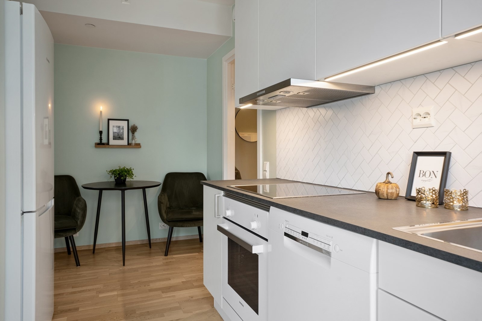 Kjøkkenet er lyst og moderne med integrerte hvitevarer, fliser og lys mellom kjøkkenbenk og overskap. Galleribilde