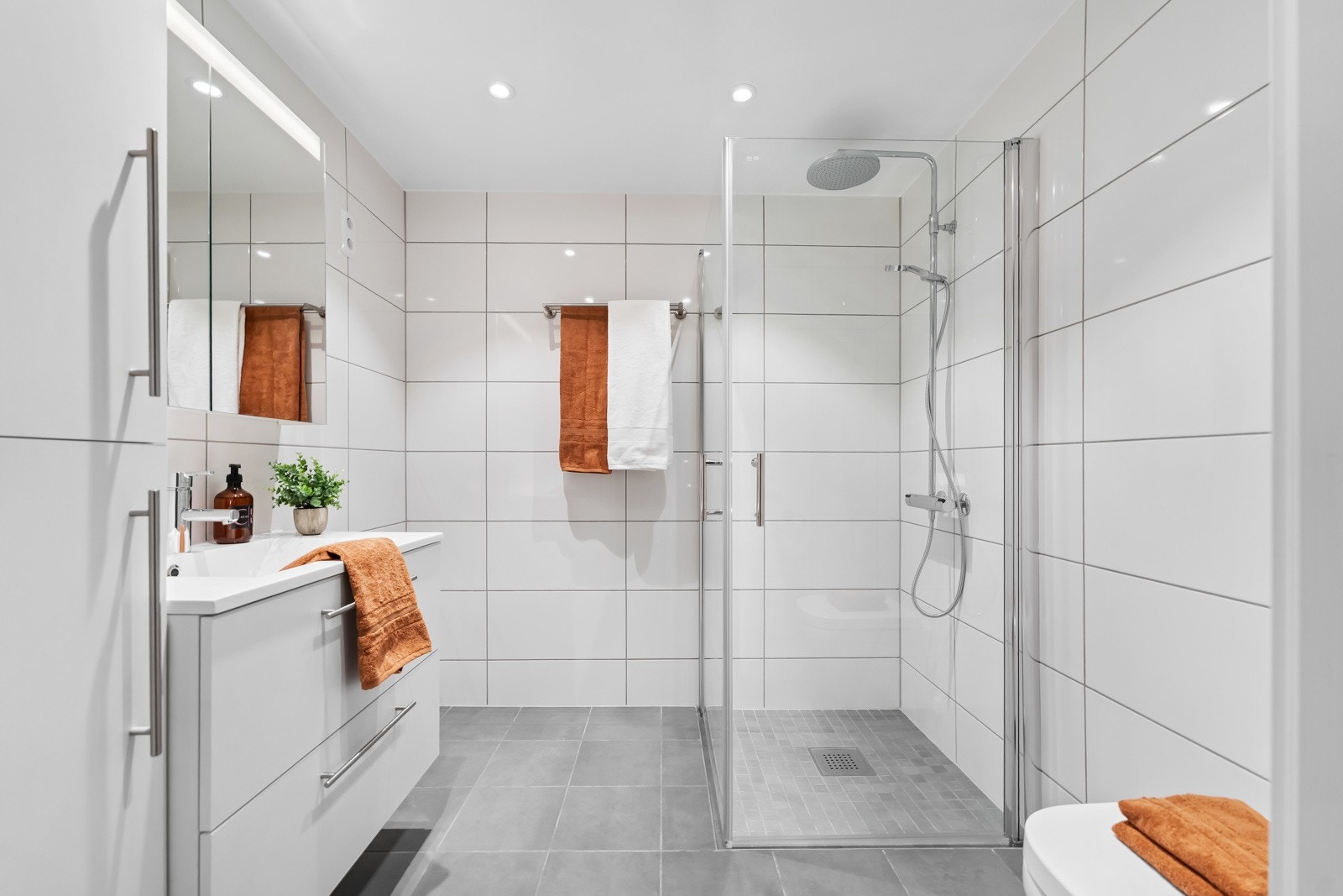 Badet er delikat og helfliset, med varme i gulv. Innredningen består av servantseksjon med skuffer, høyskap og speilskap med innfelt LED-belysning. Galleribilde