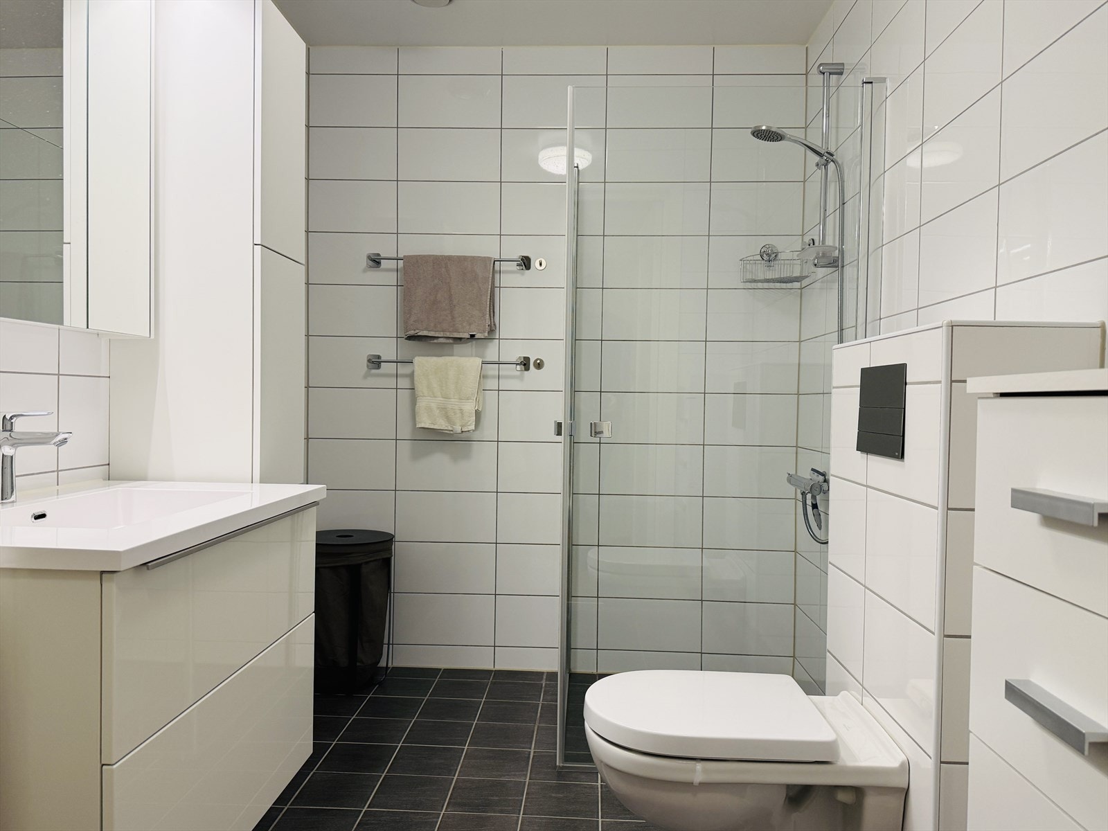 Badet er helfliset med varmekabler. Innredet med nedfelt servant i baderomsmøbel, veggmontert toalett og dusjhjørne. Galleribilde