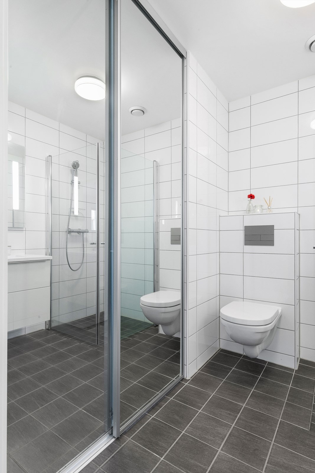 Badet er innredet med nedfelt servant i baderomsmøbel, veggmontert toalett og dusjhjørne. Galleribilde