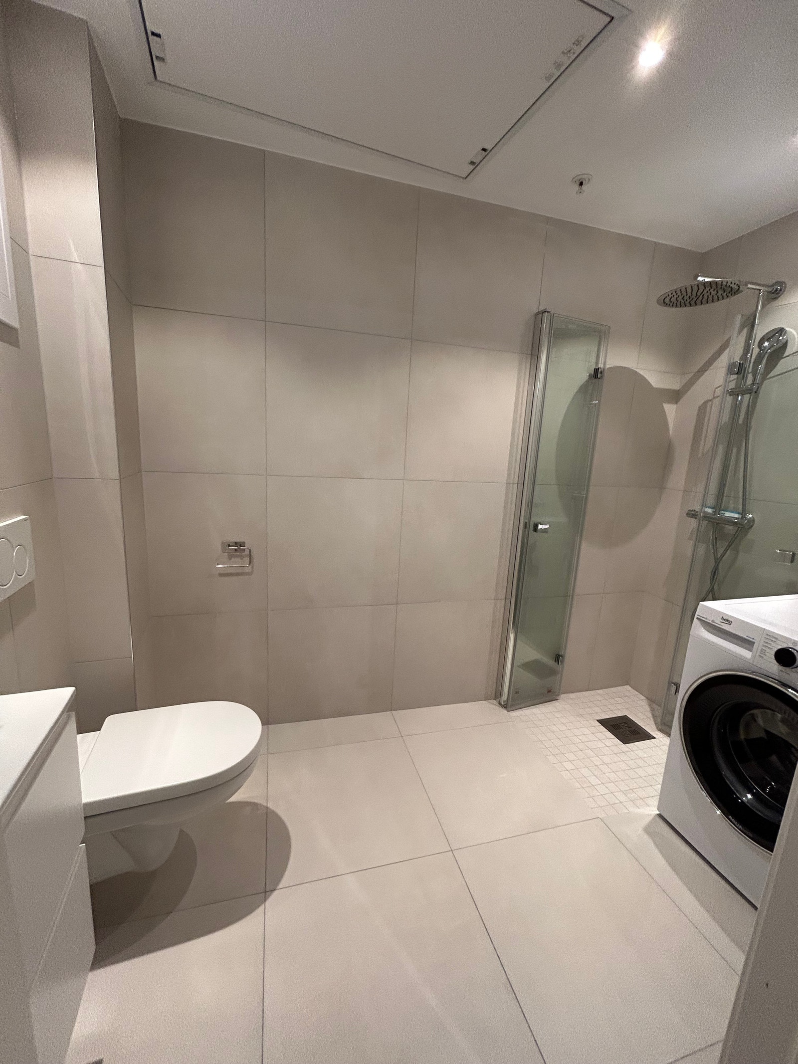 Stort flislagt dusjbad med varmekabler og vaskemaskin installert Galleribilde