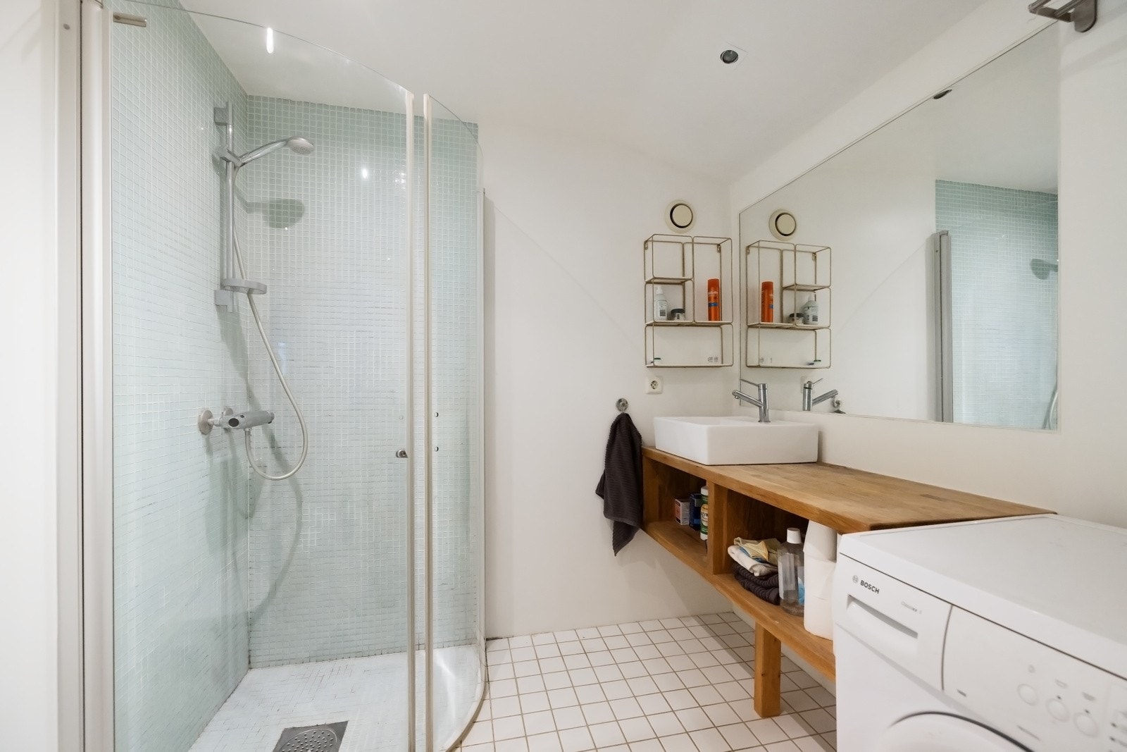 Baderom (Gjestedel), har flislagt gulv, varmekabler, og malte flater på veggene (fliser i dusjsone). Innredning med speil, downlights, opplegg for vaskemaskin, servant med innredning og dusjhjørne med innfellbare glassdører. Galleribilde