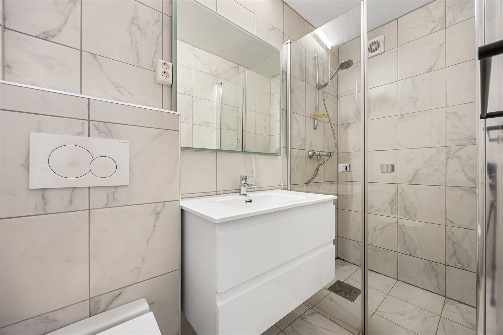 Innredningen består av vegghengt toalett, servant, speil på vegg og dusjsone med glassdører. Galleribilde