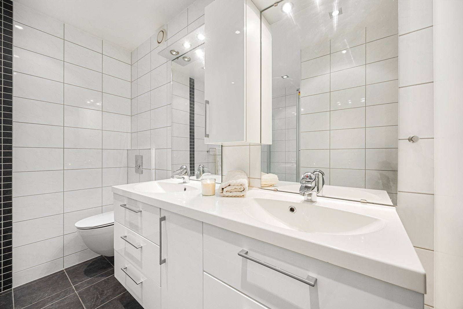 Innredningen består av vegghengt toalett, dusjhjørne med innsvingbare glassdører, dobbel servant med skuffeinnredning, høyskap og overskap. Galleribilde