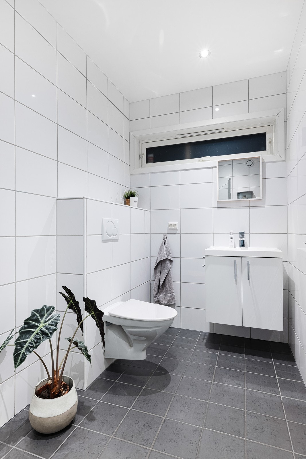 Helfliset baderom i stilrene farger med varmekabler i gulv, vegghengt toalett og servant med skap under. Galleribilde