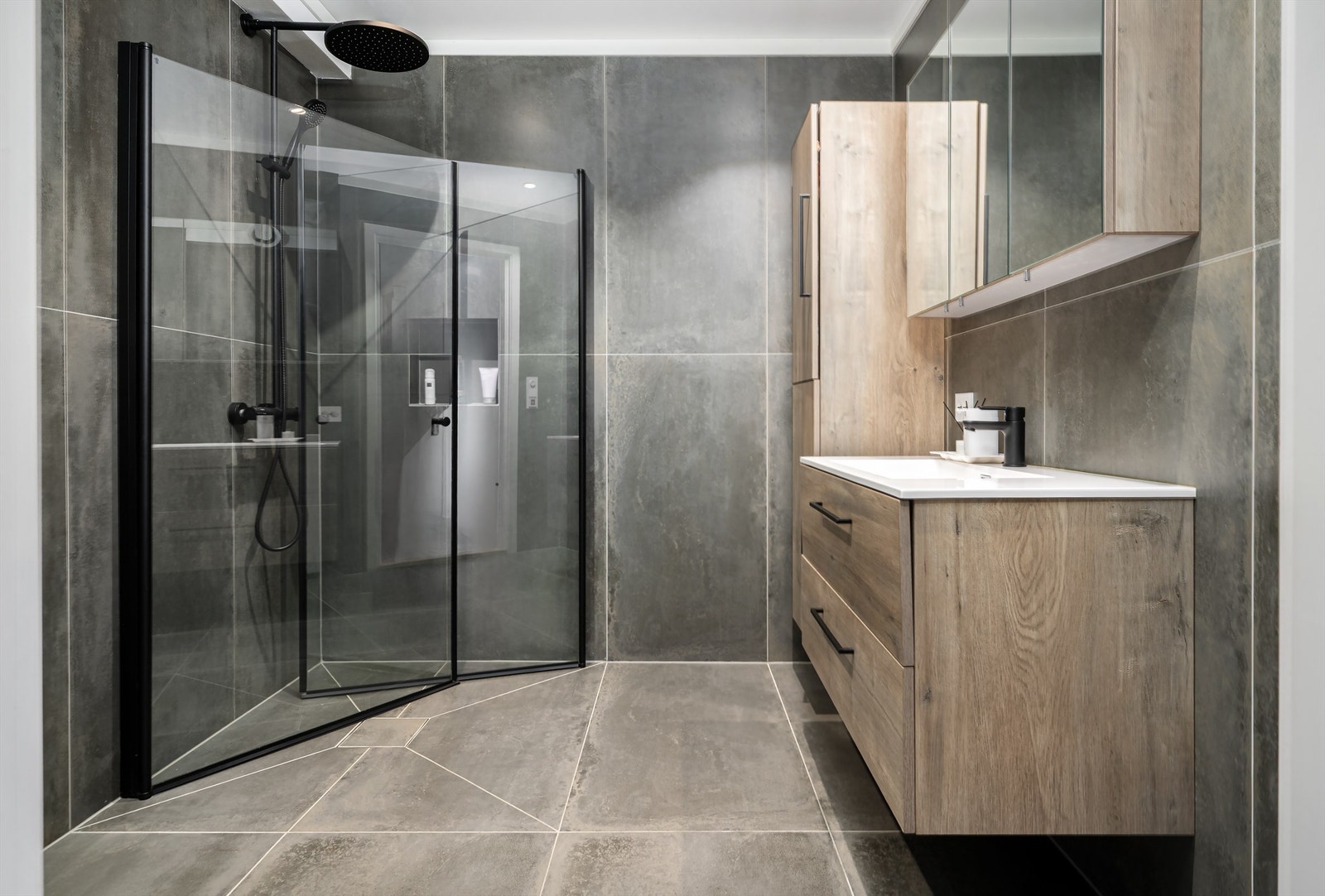 Et gjennomført og moderne baderom med store fliser og en romslig dusjsone med regnfallsdusj. Galleribilde