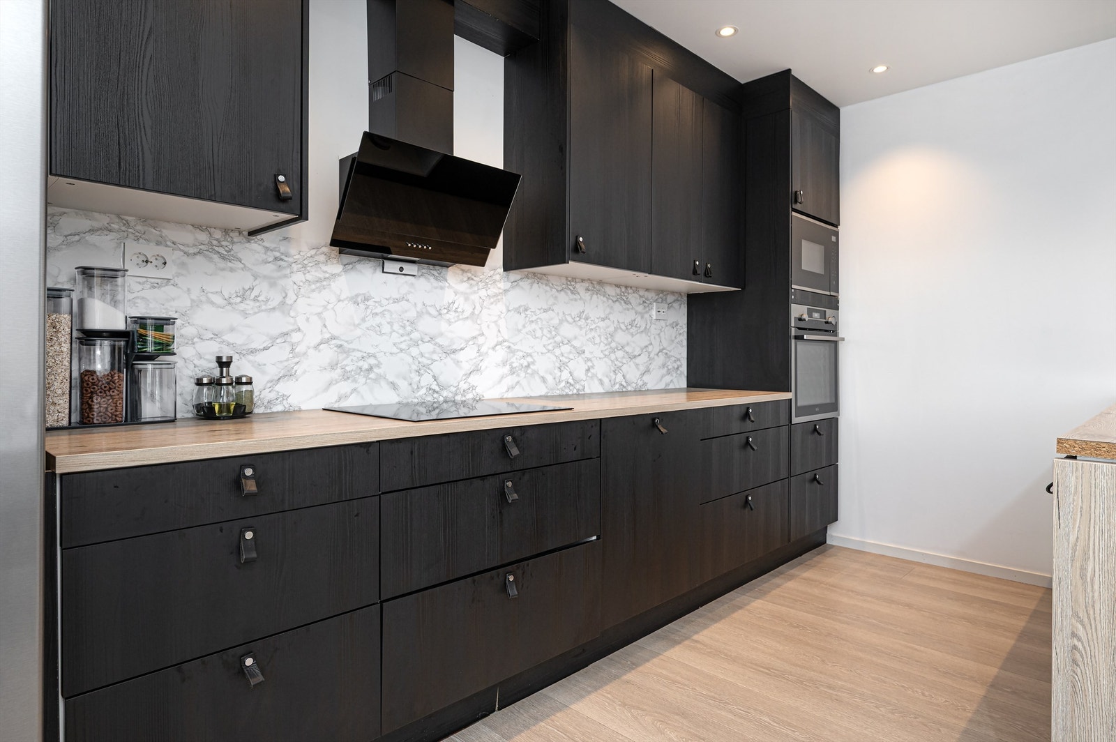 Moderne kjøkkeninnredning med mørke fronter, integrerte hvitevarer og rikelig med skap- og benkeplass. Galleribilde