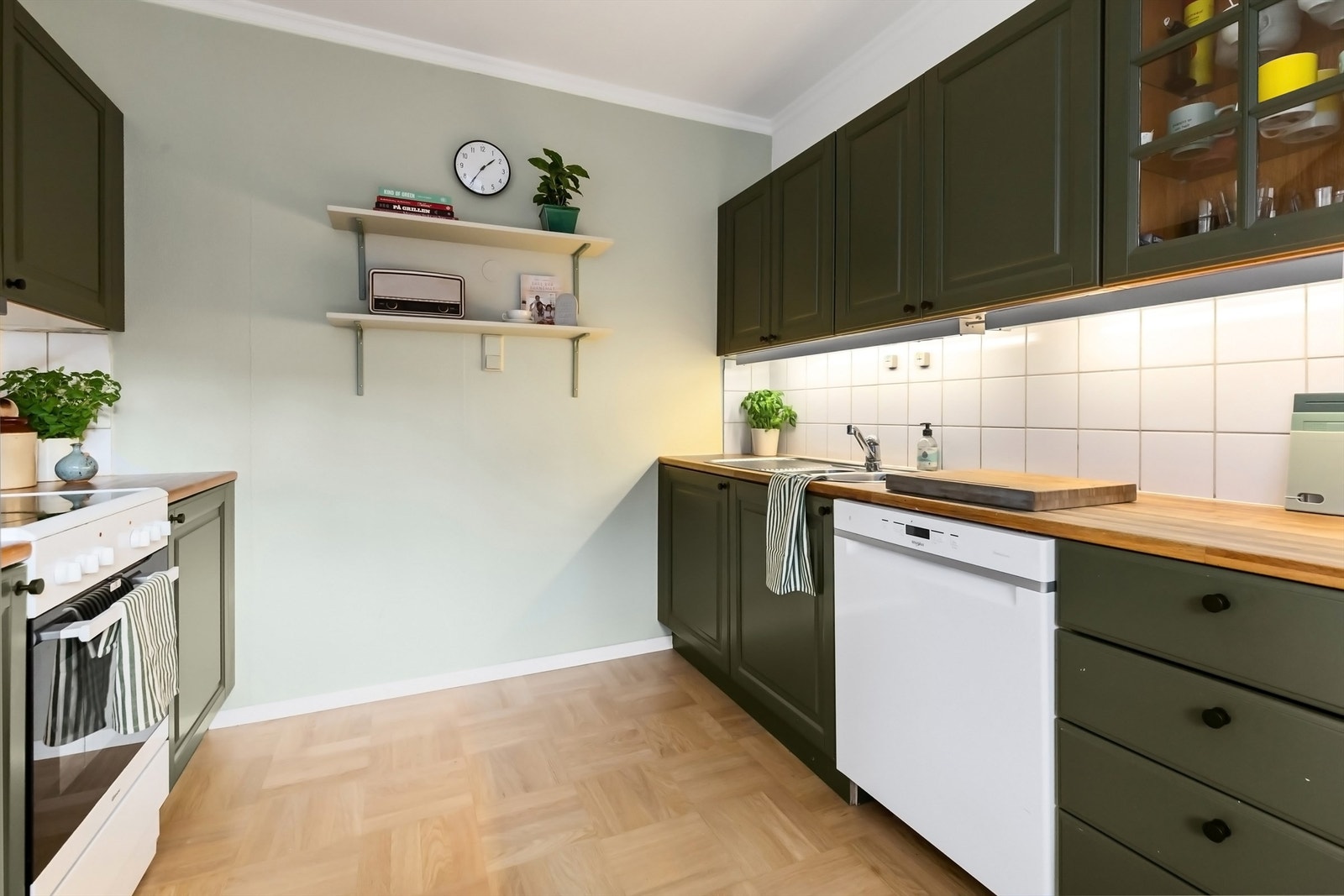 Pent kjøkken med profilerte fronter på skap og skuffer, benkeplate av tre med nedfelt kjøkkenvask og flislagt veggflate mellom benkeplate og overskap Galleribilde