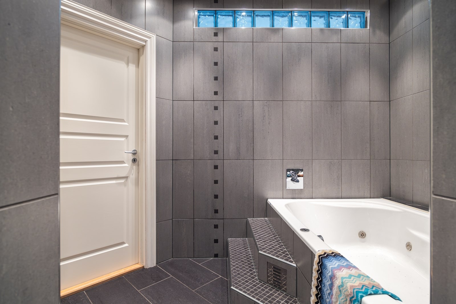 Badet er innredet med boblebad, to søyleservanter, speil, veggmontert toalett og dusjhjørne. Galleribilde