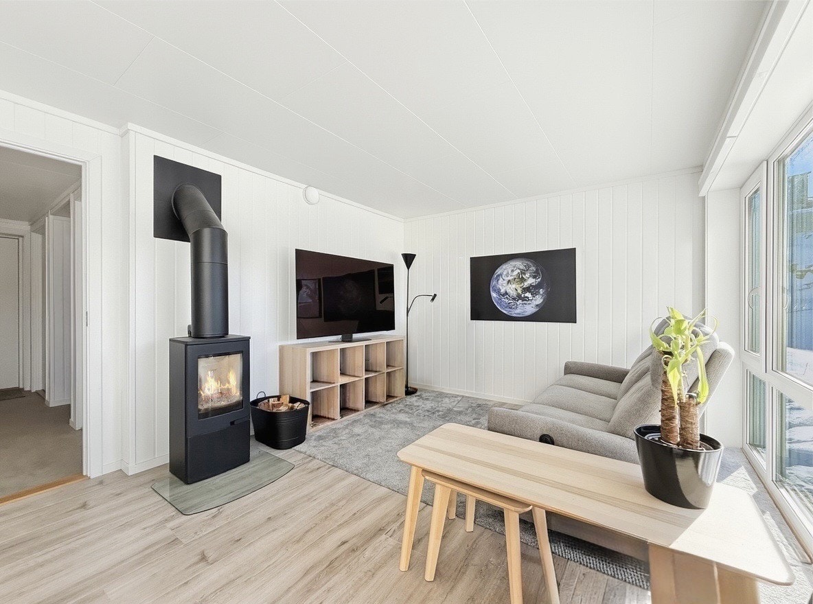 Lys stue med store vindusflater, peisovn og god plass til sofa og tv-møbler Galleribilde