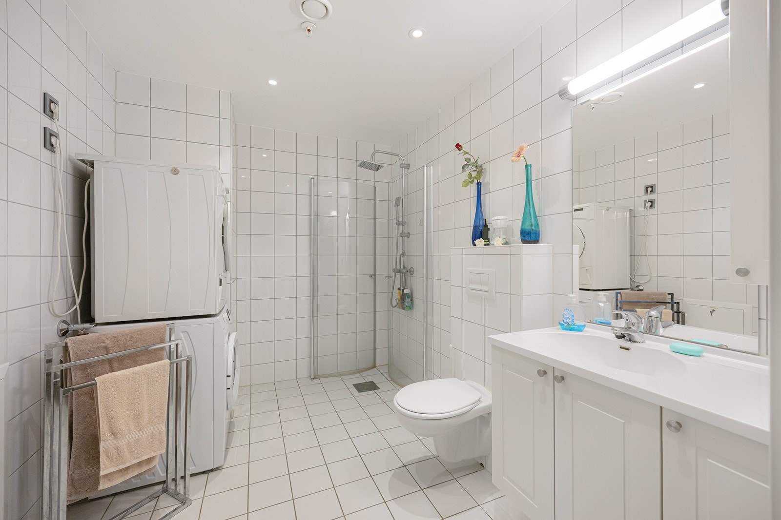 Badet har downlights i himlingen og elektriske varmekabler i gulvet. Rommet er også innredet med vegghengt toalett, speil og et hvitt skuffemøblement med heldekkende servant. Galleribilde