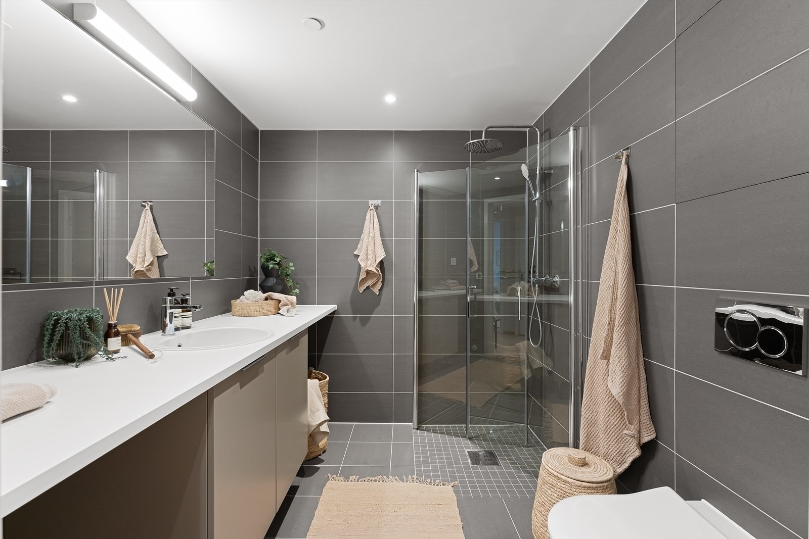 Badet er utstyrt med innredning med nedfelt servant, veggmontert toalett, dusjvegger/hjørne og opplegg for vaskemaskin under benkeplate. Galleribilde