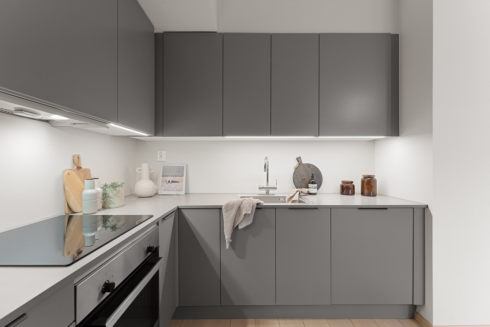 Laminat benkeplate med nedfelt stålkum og induksjonstopp, med led lys under overskap som lyser opp benkeplaten. Integrerte hvitevarer består av komfyr, oppvaskmaskin og kombindert kjøeskap/fryser. Det er avtrekk via balansert anlegg. Galleribilde