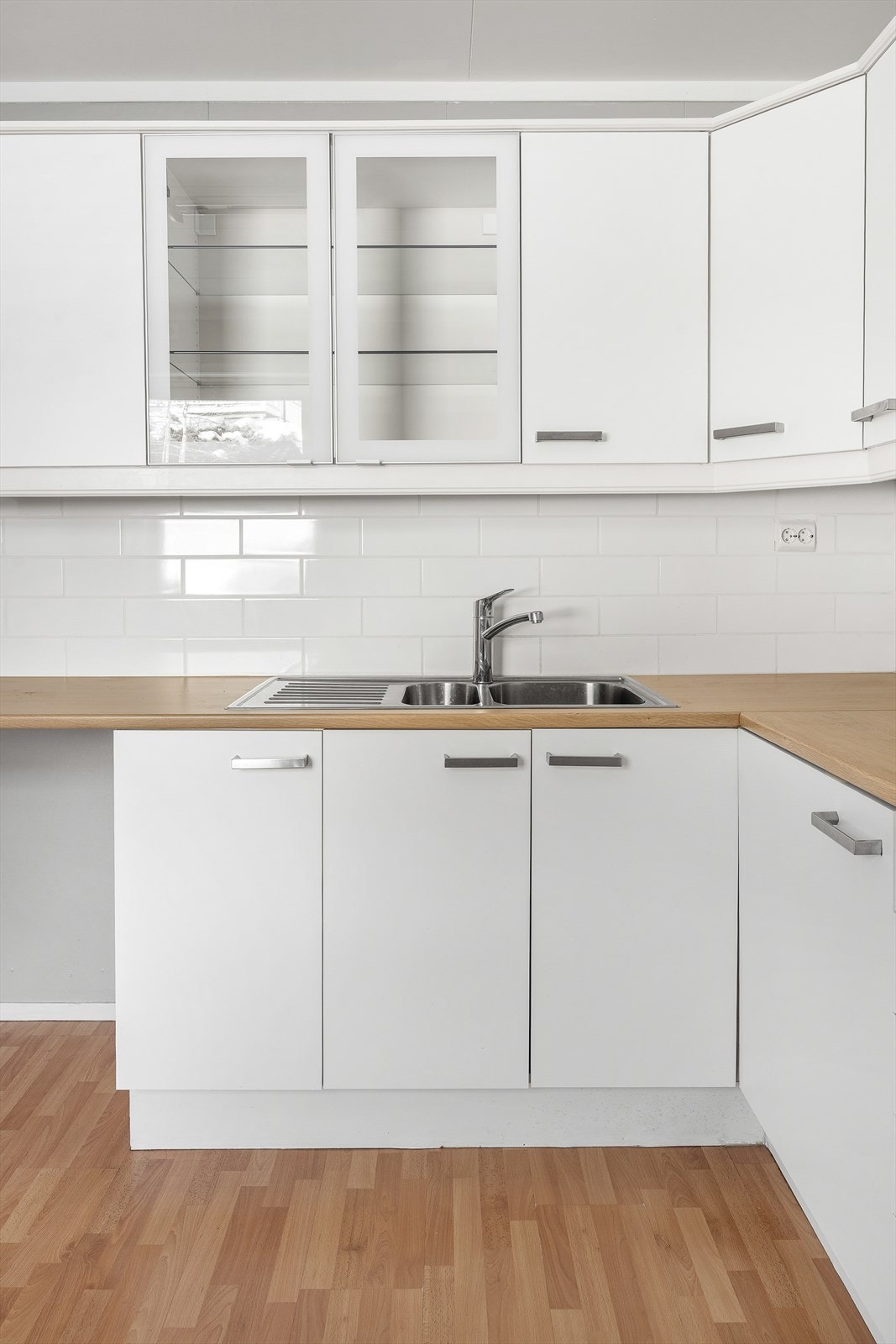 Kjøkkeninnredning i hvit, glatt utførelse med vitrineskap og laminat benkeplate. Galleribilde