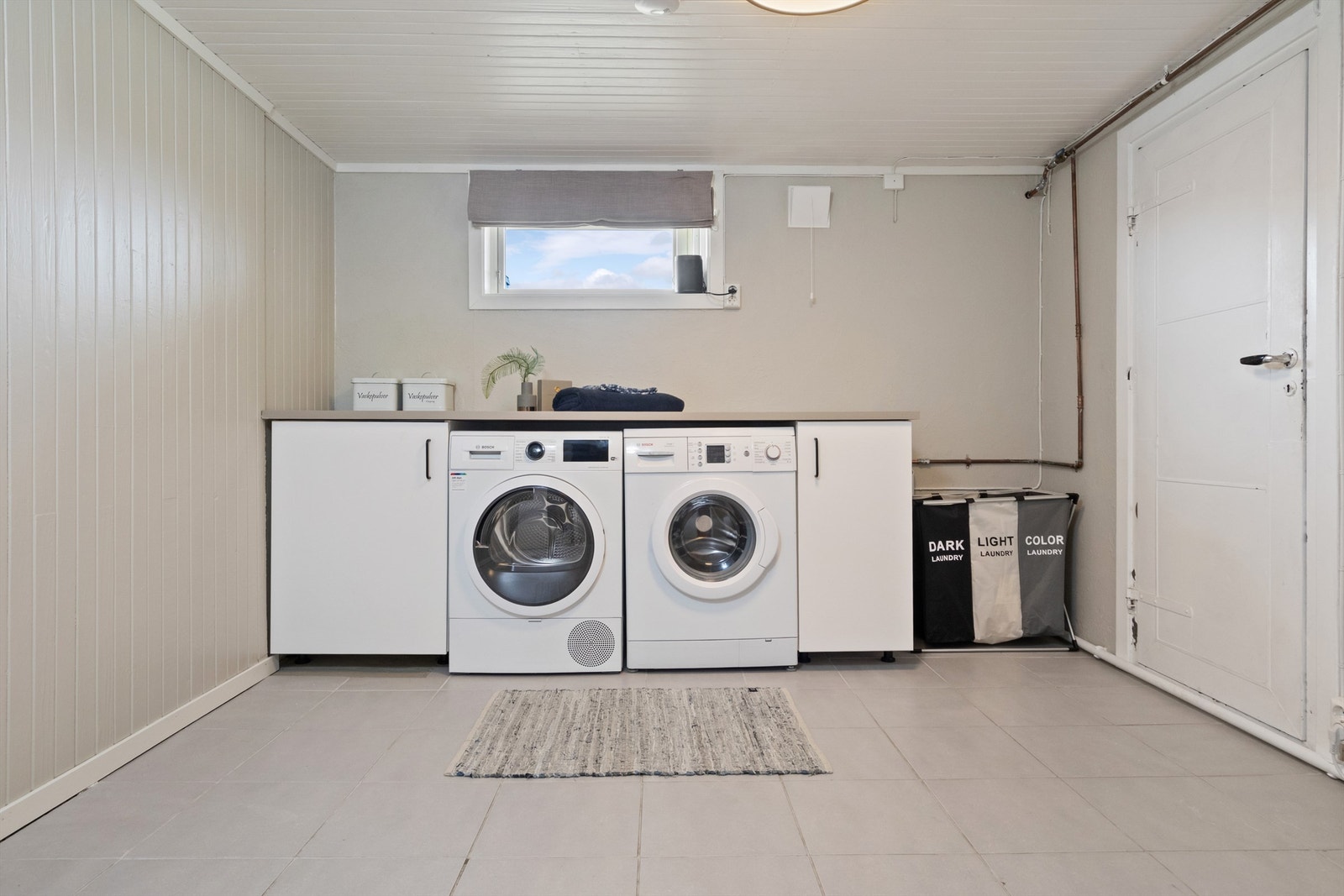 Romslig og hyggelig vaskerom. Vaskerommet har fliser på gulv, malte mur- og panelvegger, samt innredning med skap, arbeidsbenk, opplegg for vaskemaskin/tørketrommel og wc. Galleribilde