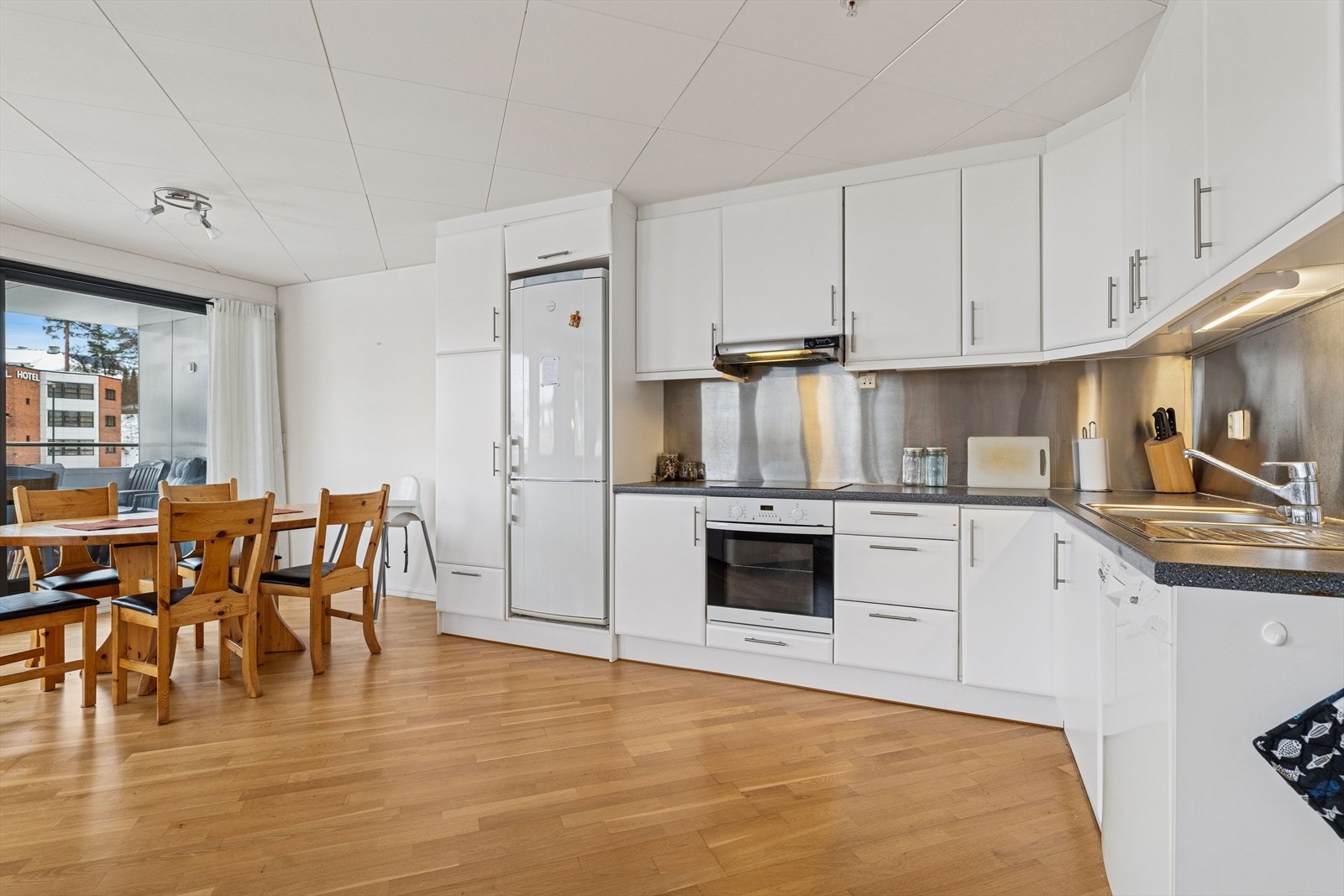 Lyst og moderne kjøkken med glatte fronter, god benkeplass og naturlig lys fra store vinduer. Galleribilde