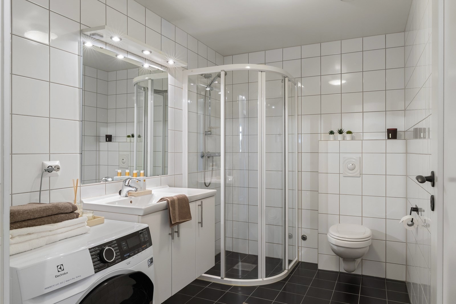 Badet har en romslig utforming som gir god plass til nedfelt servant, veggmontert toalett, dusjdører og opplegg for vaskemaskin. For ekstra komfort er det også gulvvarme Galleribilde