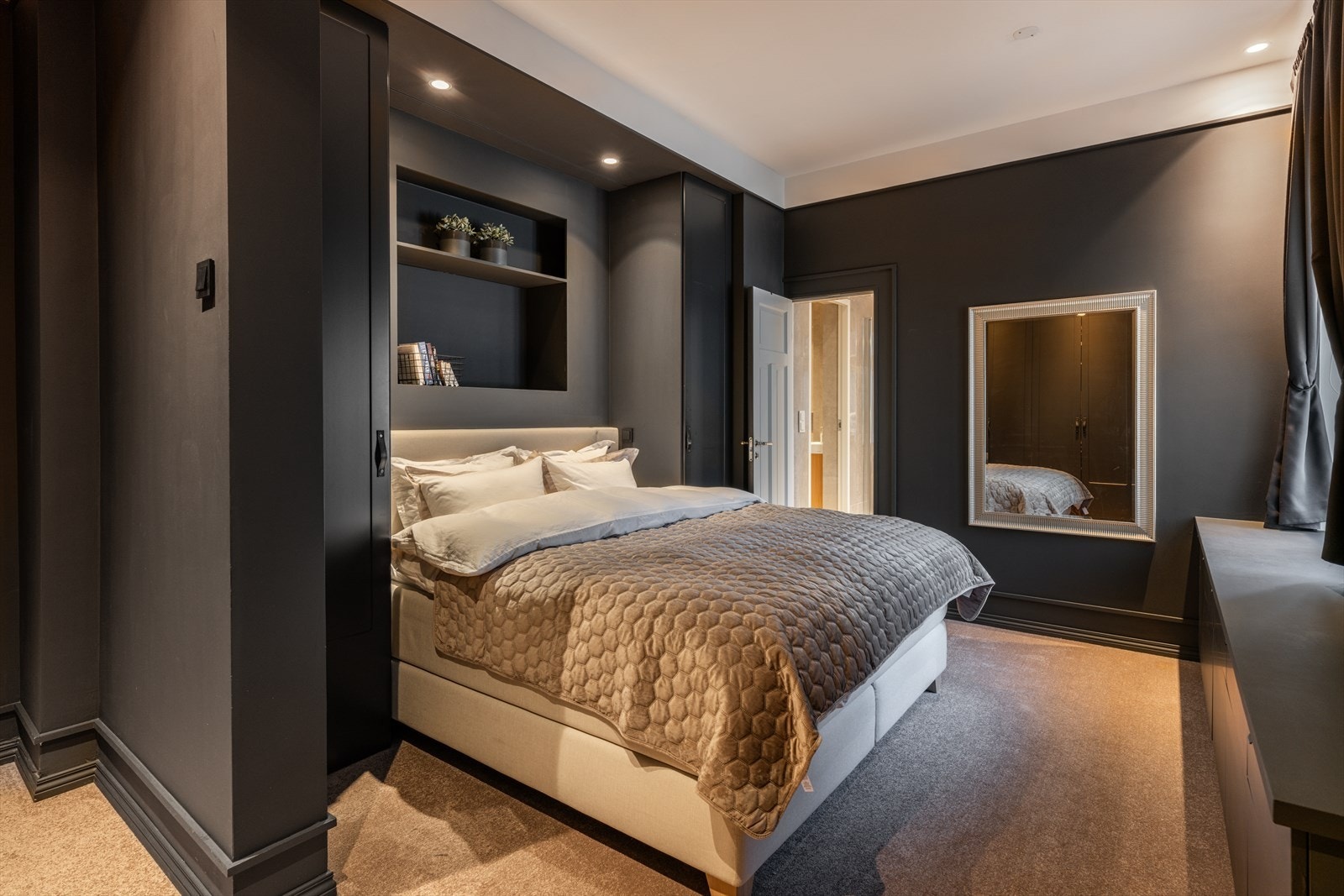 Hovedsoverommet fremstår som en elegant og sofistikert suite, utført i dype, harmoniske fargetoner og med vegg-til-vegg-teppe som tilfører rommet en lun og eksklusiv karakter. Galleribilde