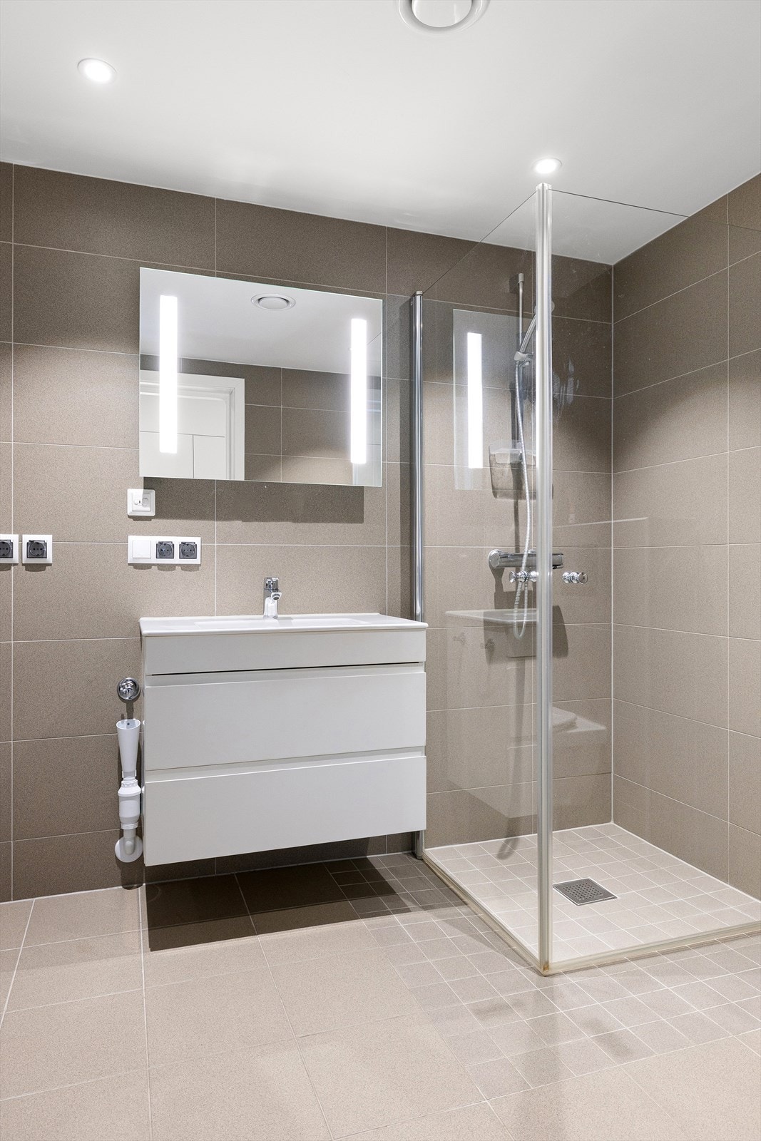 Badet er innredet med servant i baderomsinnredning, speil med integrert belysning, dusjhjørne med innfellbare glassvegger og opplegg for vaskemaskin. Galleribilde