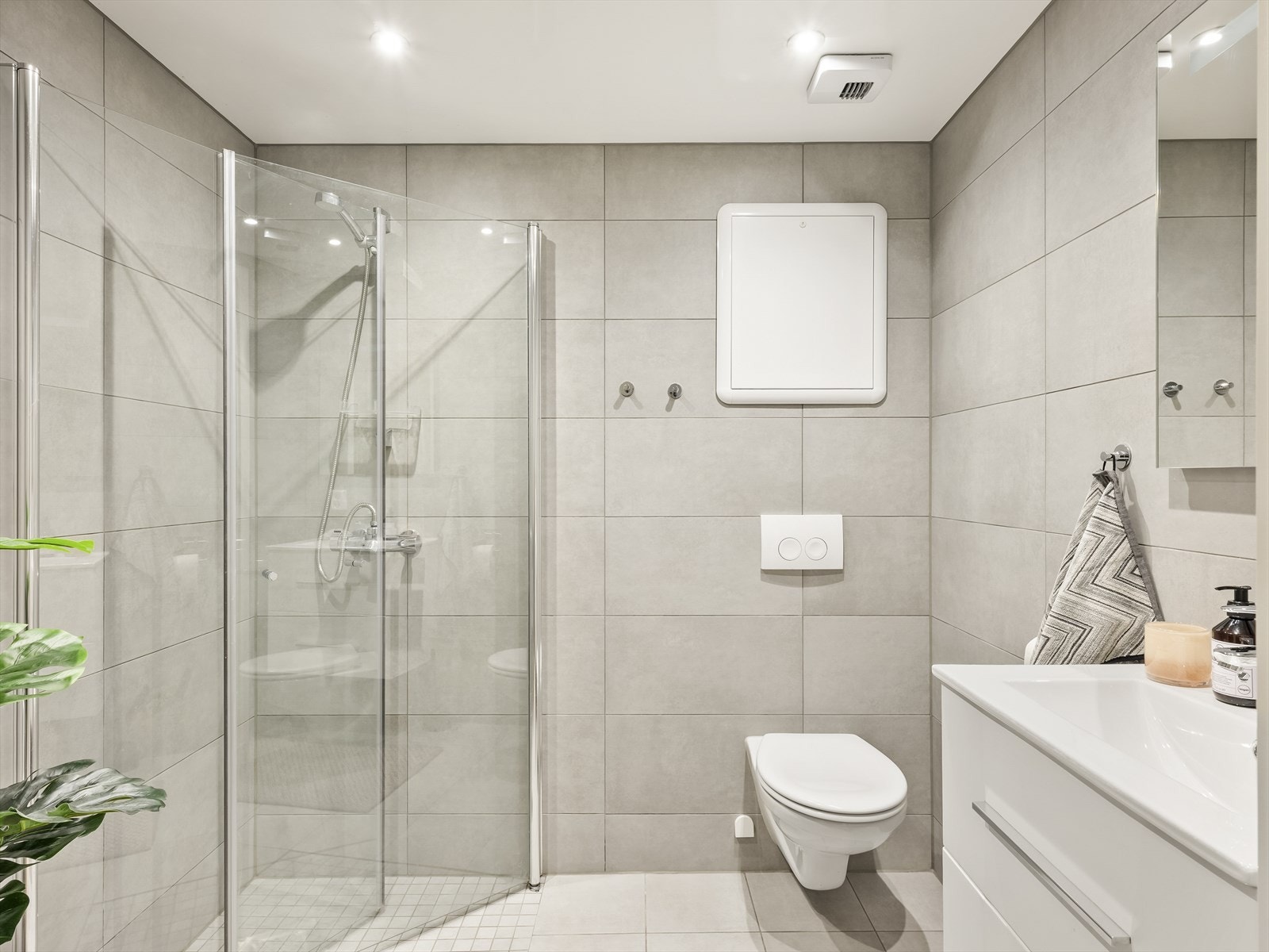 Flislagt bad med vegghengt toalett, dusjvegger i glass og opplegg for vaskemaskin. Galleribilde