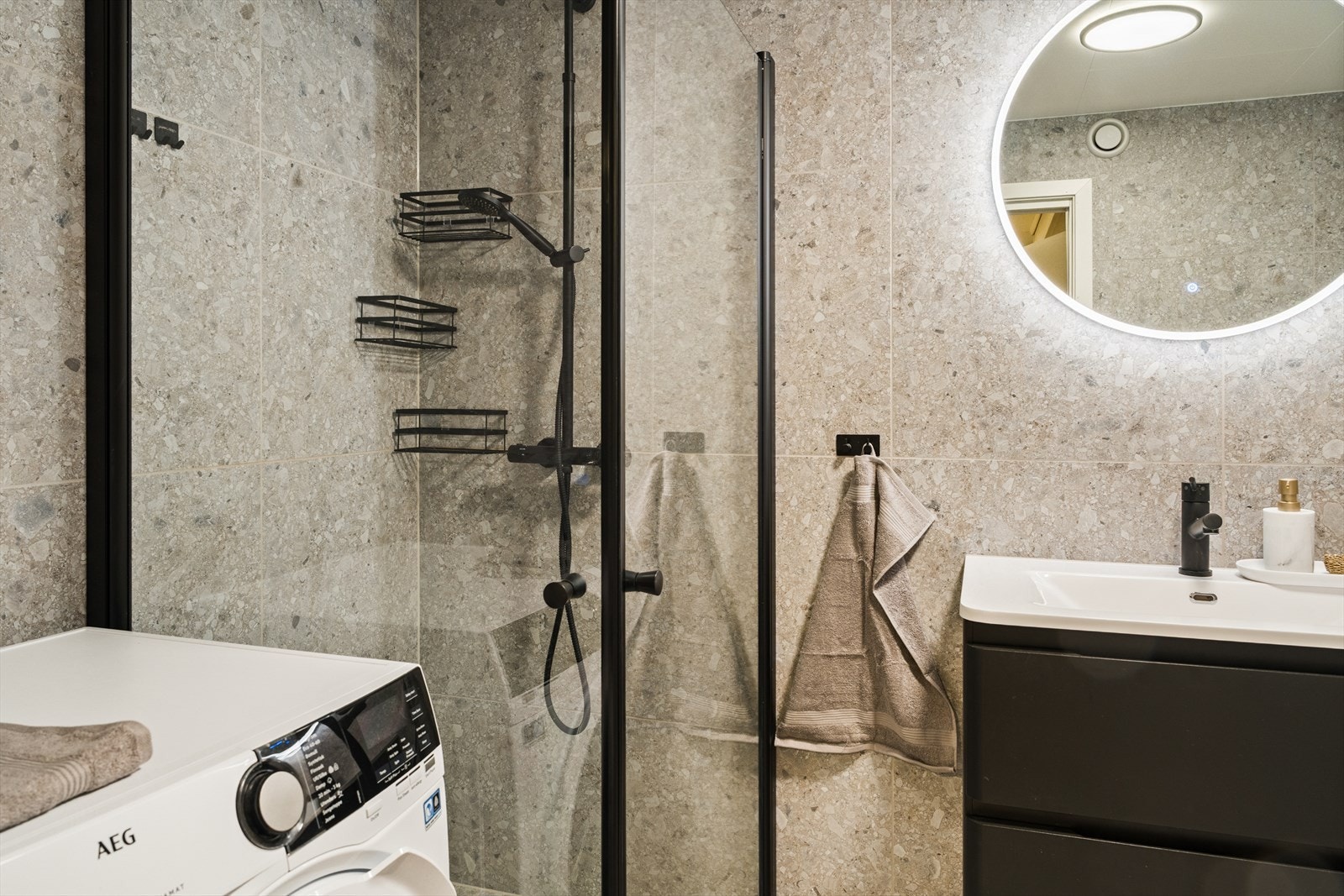 Badet inneholder innredning med nedfelt servant, toalett, dusjvegger samt opplegg for vaskemaskin Galleribilde