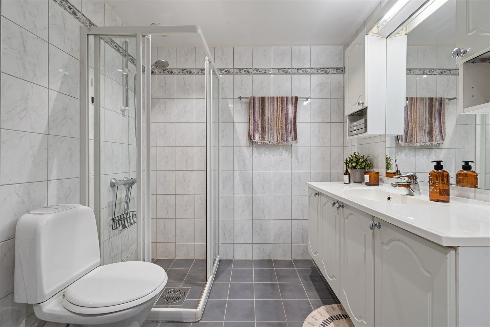 Dusjvegger i glass og gulvstående toalett. Baderomsinnredning med underskap og overskap. Speil med belysning. Downligts i taket. Galleribilde