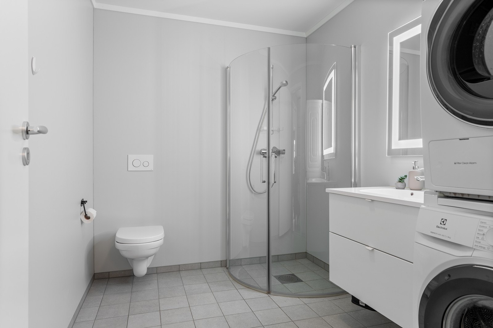 Flott bad medvegghengt wc, dusj med glassdører samt vegghengt baderomsinnredning med underskuffer og nedfelt servant. Det er opplegg for vaskemaskin og tørketrommel Galleribilde