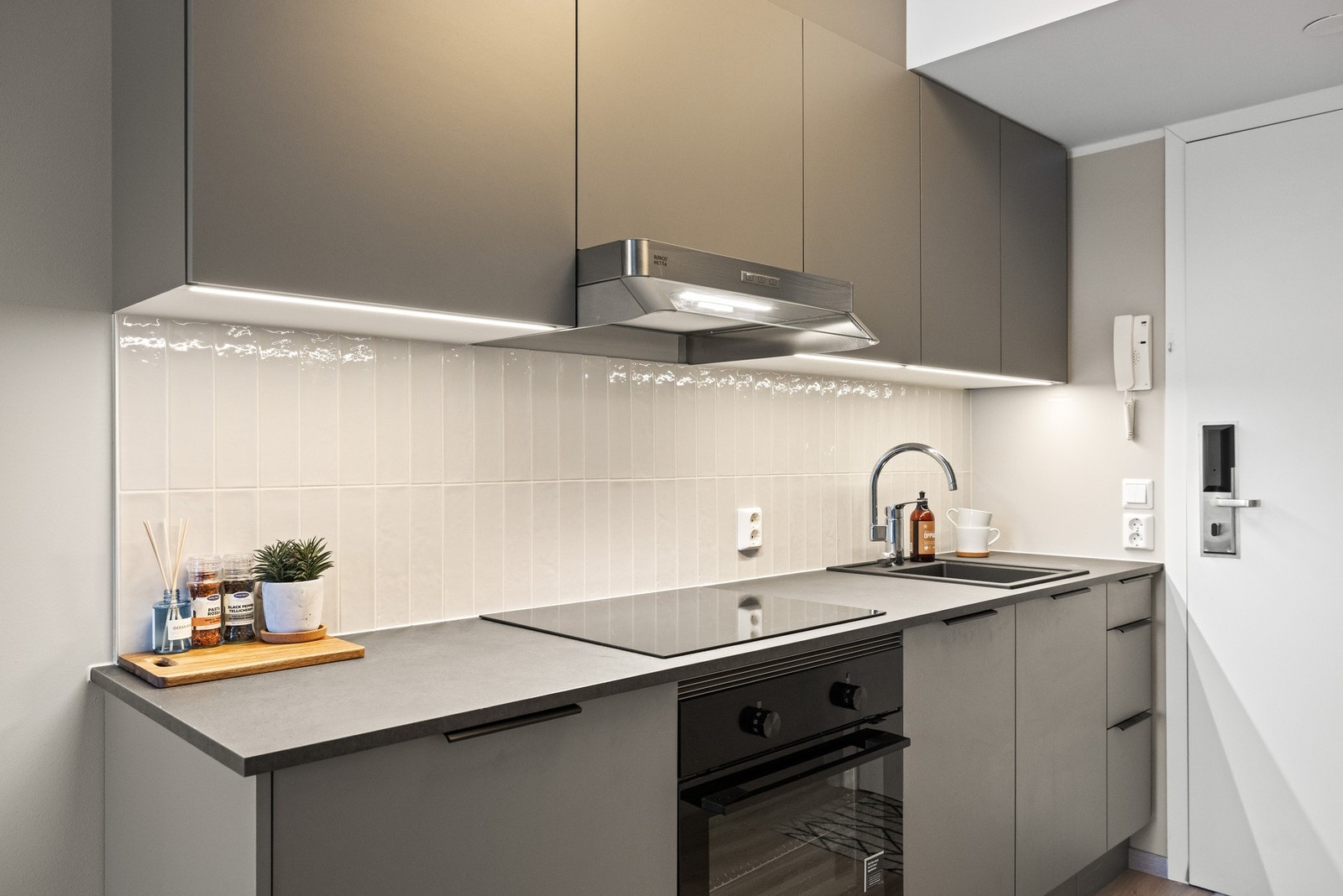 Kjøkkenet er et lekkert, grått HTH-kjøkken spesialtilpasset leiligheten, med glatte fronter, takforing og integrert LED-belysning under overskapene. Galleribilde