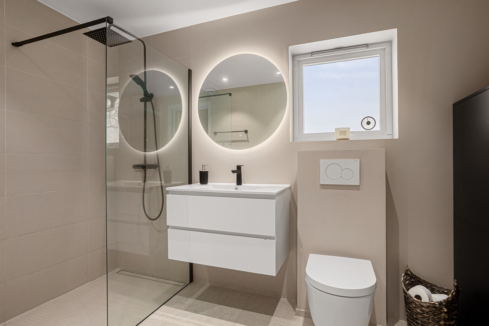 Innredet med dusjhjørne med skillevegg av glass, vegghengt toalett samt vegghengt servantskap med speil og integrert belysning Galleribilde