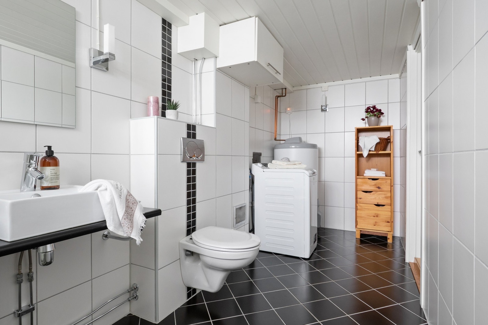 Rommet fremstår som velholdt og har et moderne uttrykk med hvite fliser på veggene og sorte fliser på gulvet. Det er også opplegg for vaskemaskin. Galleribilde