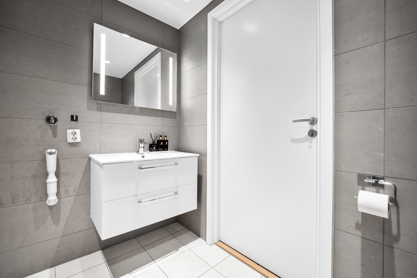 Innredet med servant med skuffer, speil med belysning, dusjhjørne og vegghengt toalett. Galleribilde