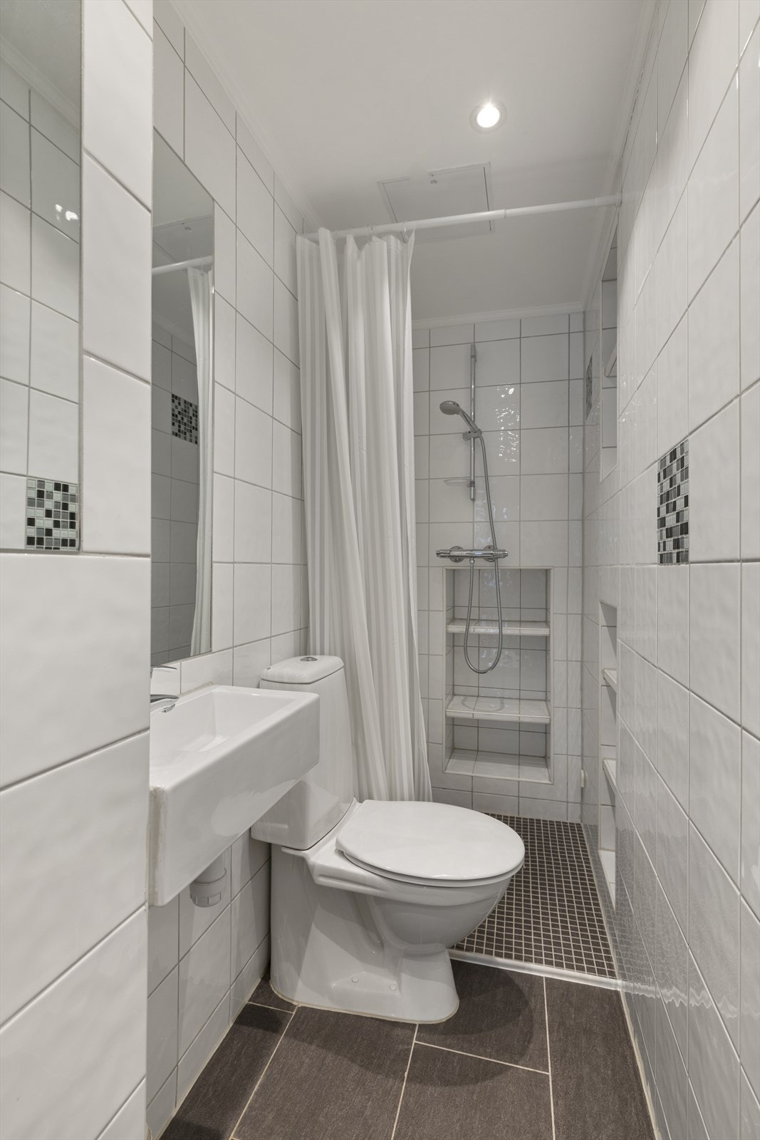 Flislagt bad med servant, toalett og dusjvegger/hjørne. Malt himling med downlights. Elektriske varmekabler på gulv. Elektrisk styrt vifte. Tilluft via spalte ved dørterskel. Det er lagringshems over bad. Galleribilde