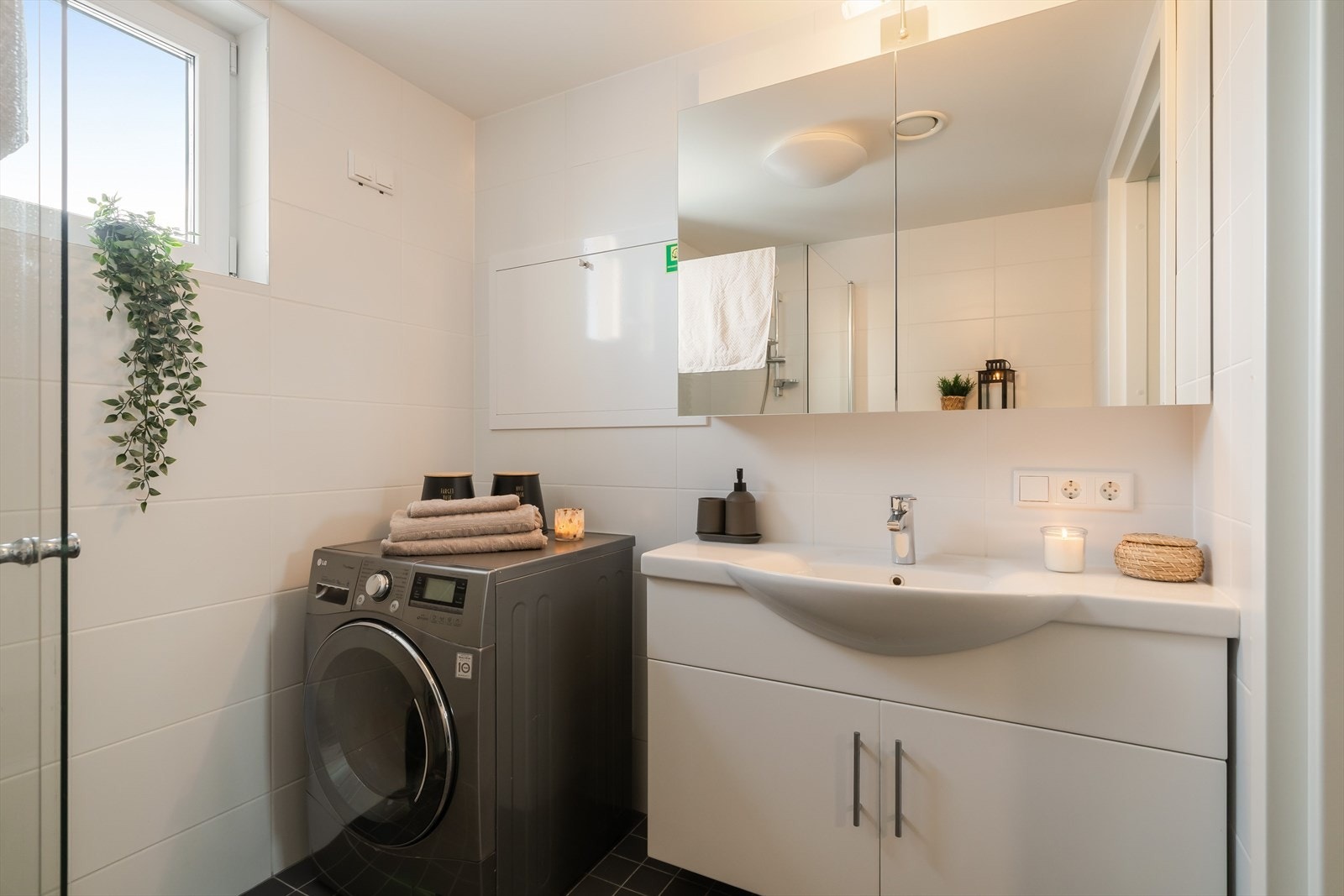 Rommet har dusjløsning med glassvegg, servant med møbel og speil med belysning. Det er også opplegg og plass til vaskemaskin, noe som gjør badet ekstra funksjonelt i hverdagen. Galleribilde