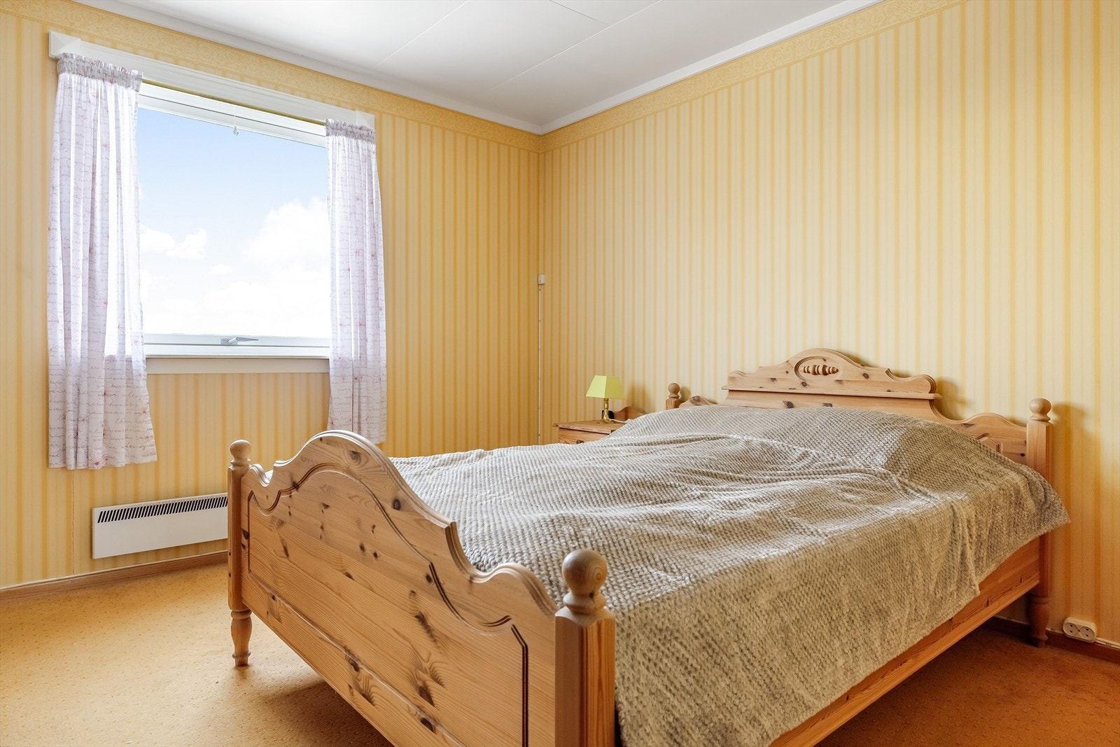 Soverom 1 har lunt teppe på gulv, tapetserte vegger og stort vindu fra 2011. Galleribilde