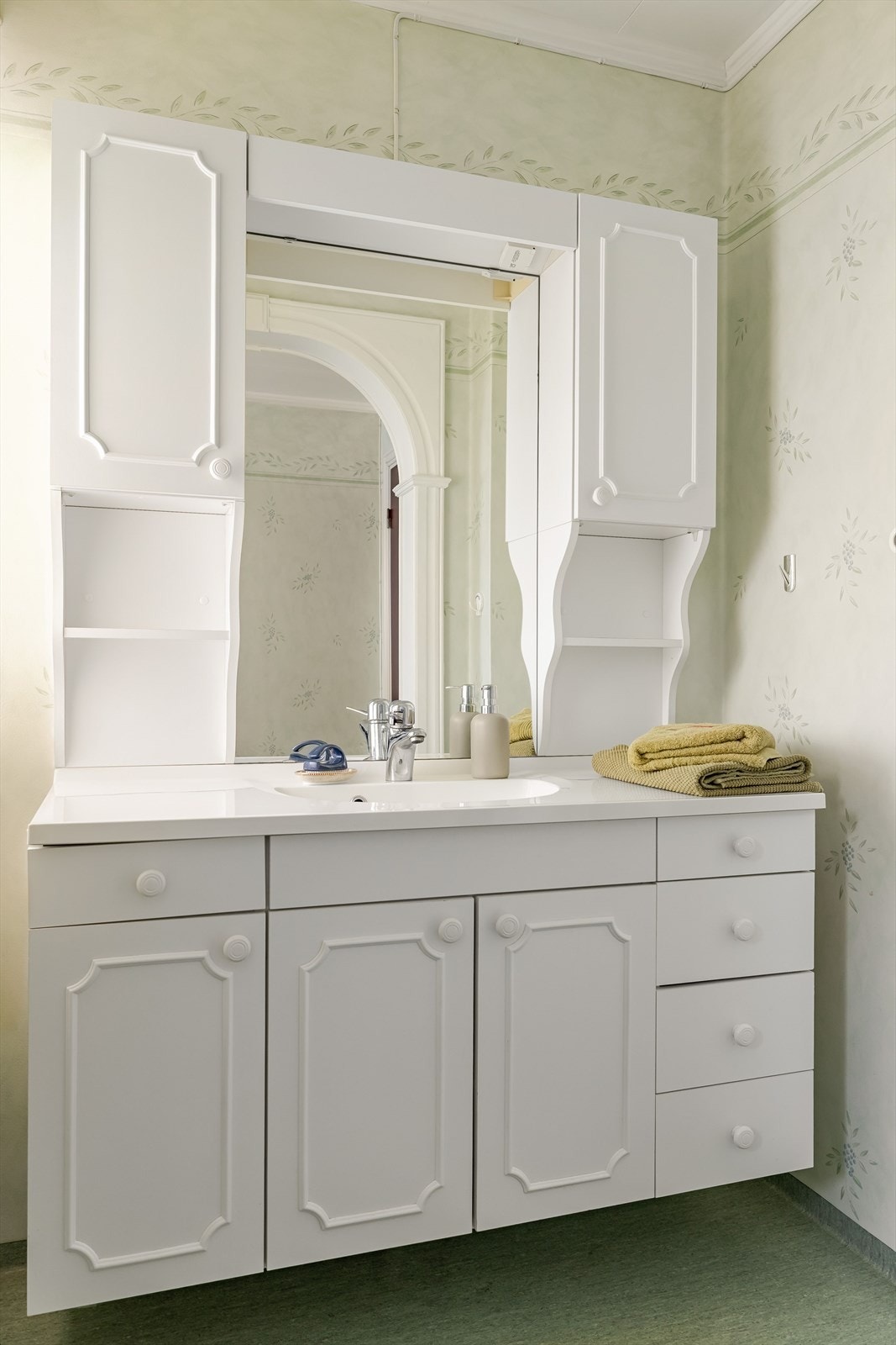 Lys baderomsinnredning med heldekkende servant, speil med belysning og vegghengte skap over. Galleribilde