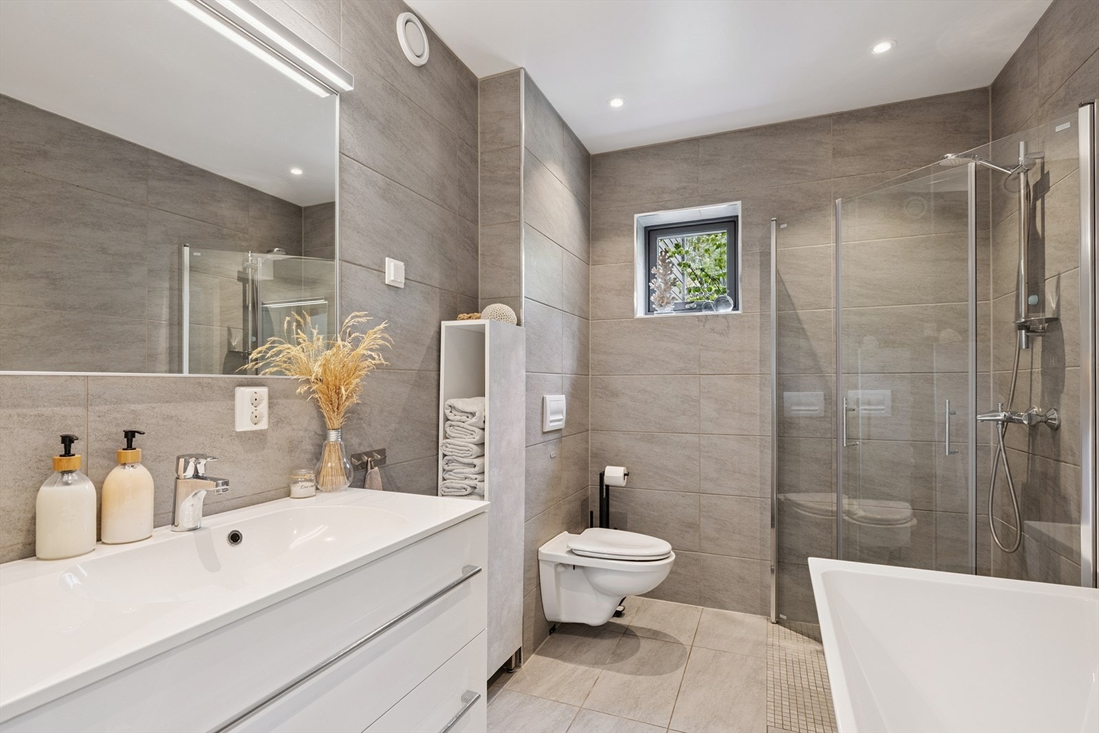 Moderne og delikat flislagt bad med dusjnisje, badekar, vegghengt wc og baderomsinnredning m/vask Galleribilde