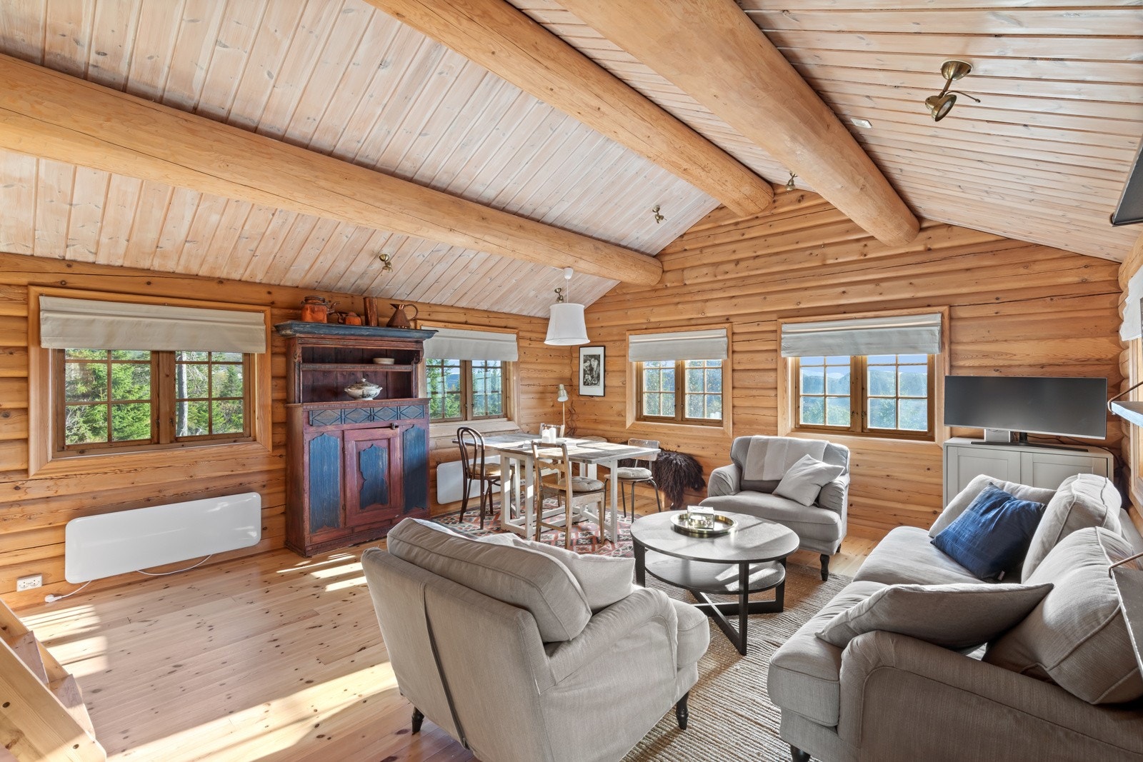 Romslig stue med raustet himling og synlige robuste takåser i rundtømmer. Galleribilde