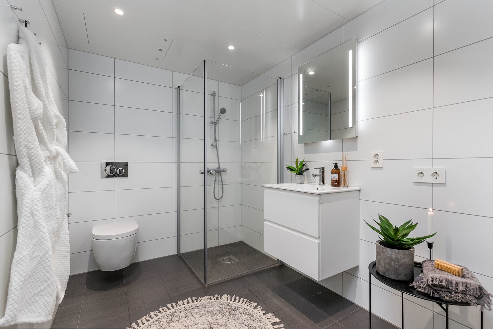 Delikat og smakfullt bad fra 2023 med flislagte overflater og varme i gulv. Moderne skuffeinnredning med servant, samt speil med belysning over servant. Galleribilde