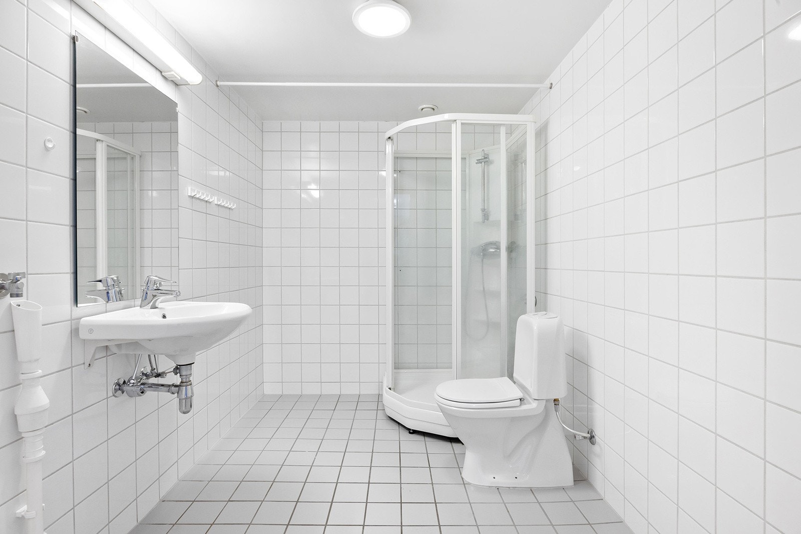 Lyst og romslig flislagt bad med gulvvarme og en innredning bestående av servant, dusjkabinett og gulvmontert toalett. Galleribilde