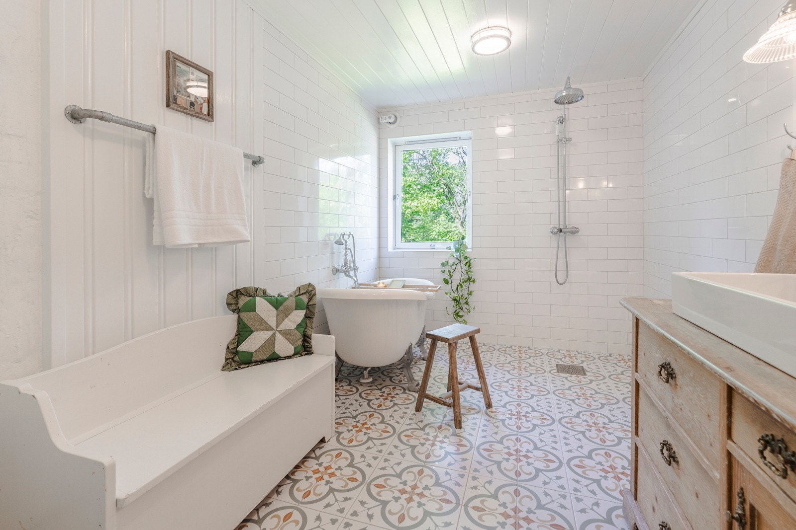 Stort, flott og flislagt bad som er innredet med badekar, dusj, servant på benk med skuffer, veggspeil og toalett. Galleribilde