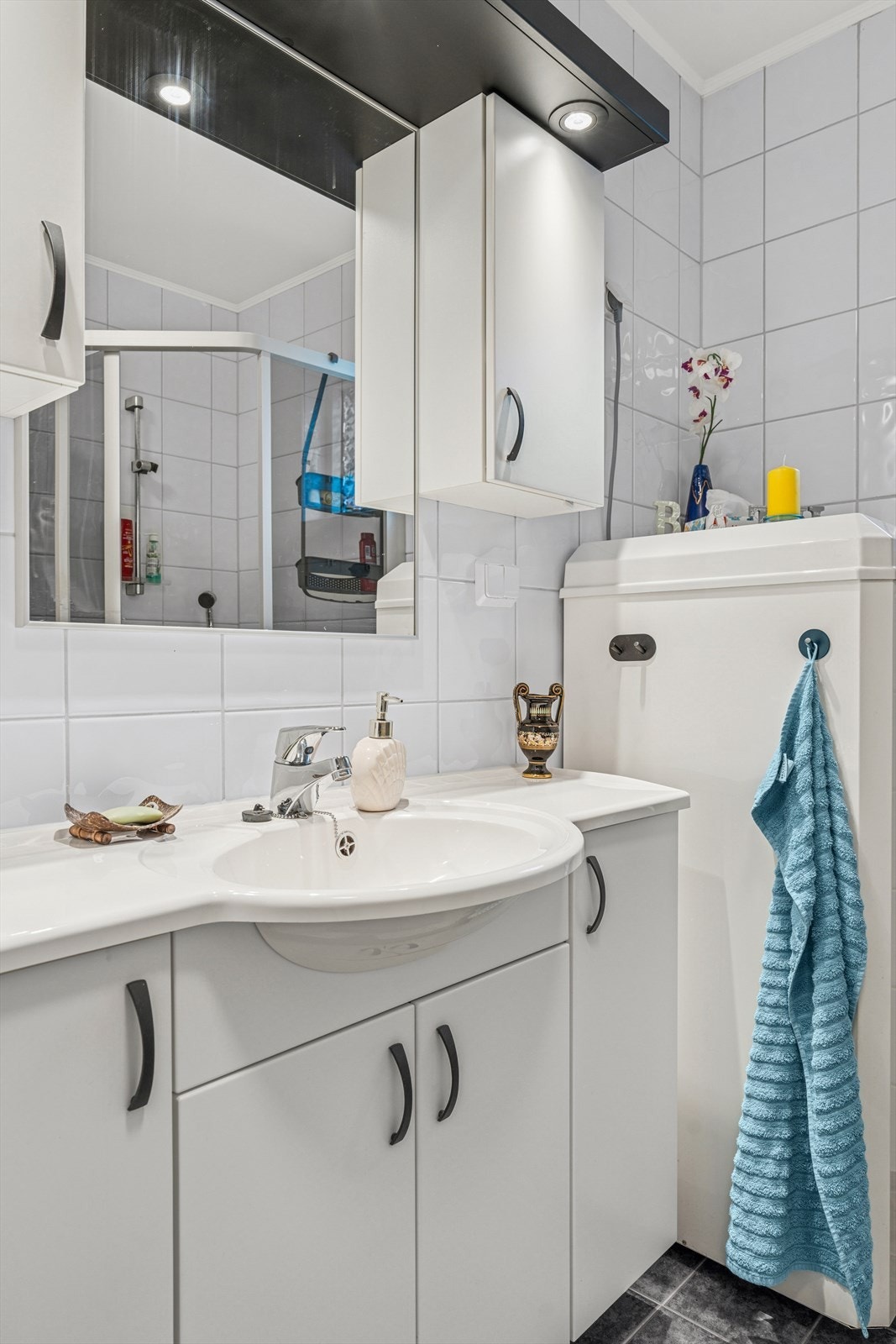 Badet har en innredning med nedfelt servant, speil med overliggende lys, toalett og dusjvegger/hjørne. Galleribilde