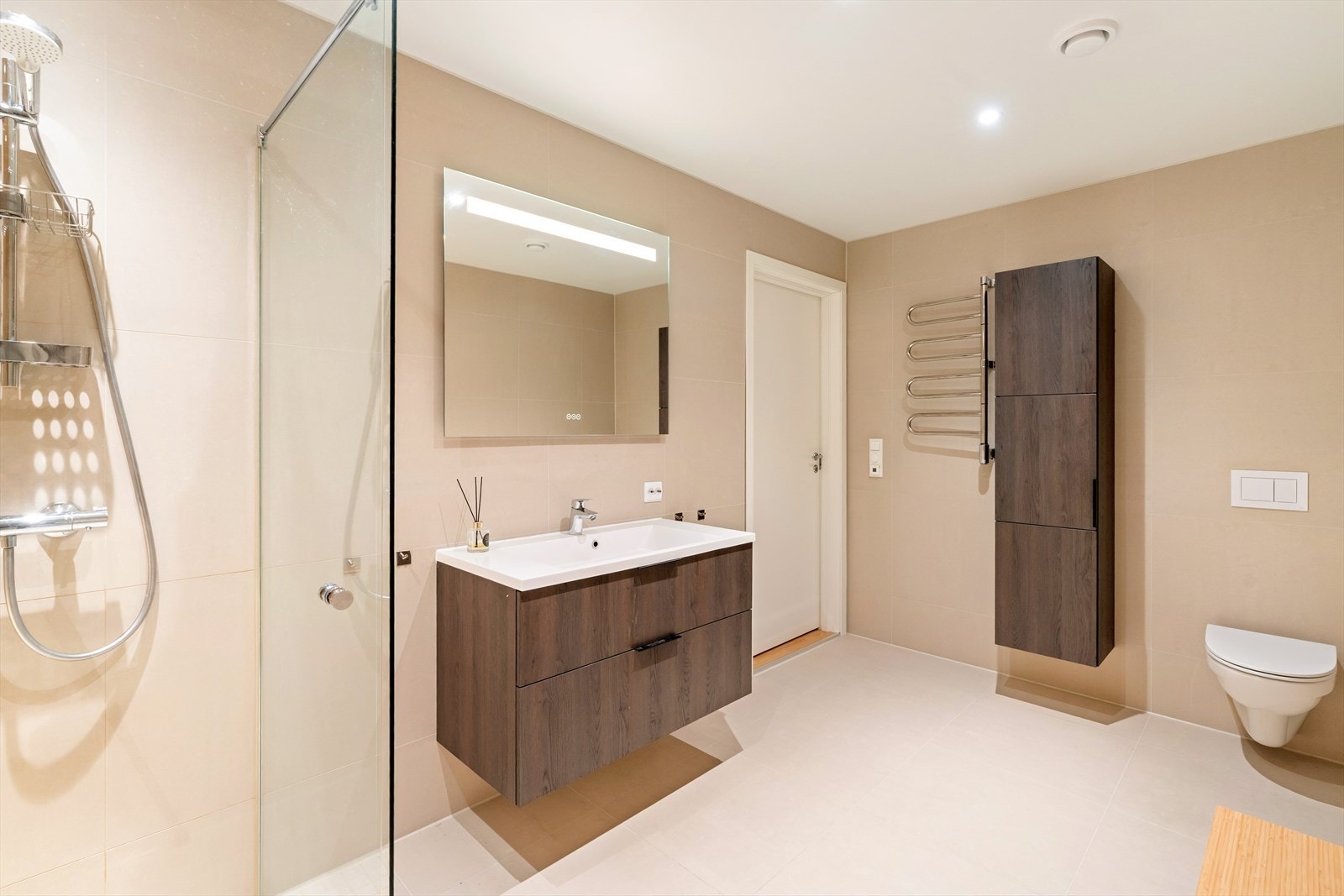 Bad i første etasje - Skuffeseksjon med vask og vegghengt speil med lys. Vegghengt toalett og dusj. Veggskap i samme interiør medfølger også. Håndkletørker med varme. Galleribilde