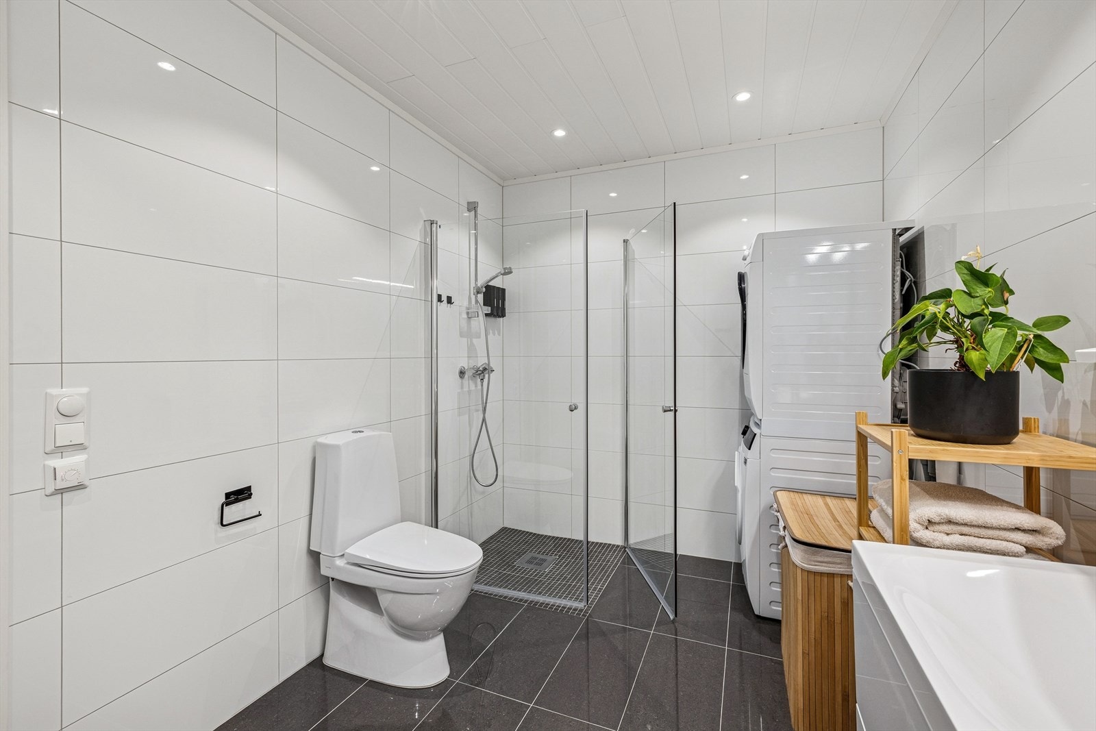 Rommet er innredet med Lind baderomsinnredning med doble servanter og underskap, speil med belysning, dusjvegger og et gulvmontert toalett. Det er varme i gulvet og opplegg for vaskemaskin. Galleribilde