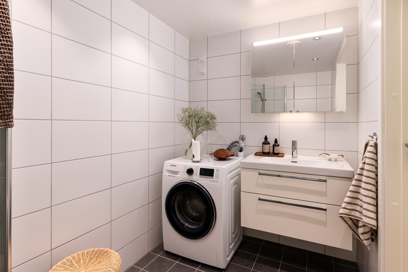 Delikat flislagt bad med hvite veggfliser og mørke gulvfliser som gir en stilren kontrast. Galleribilde